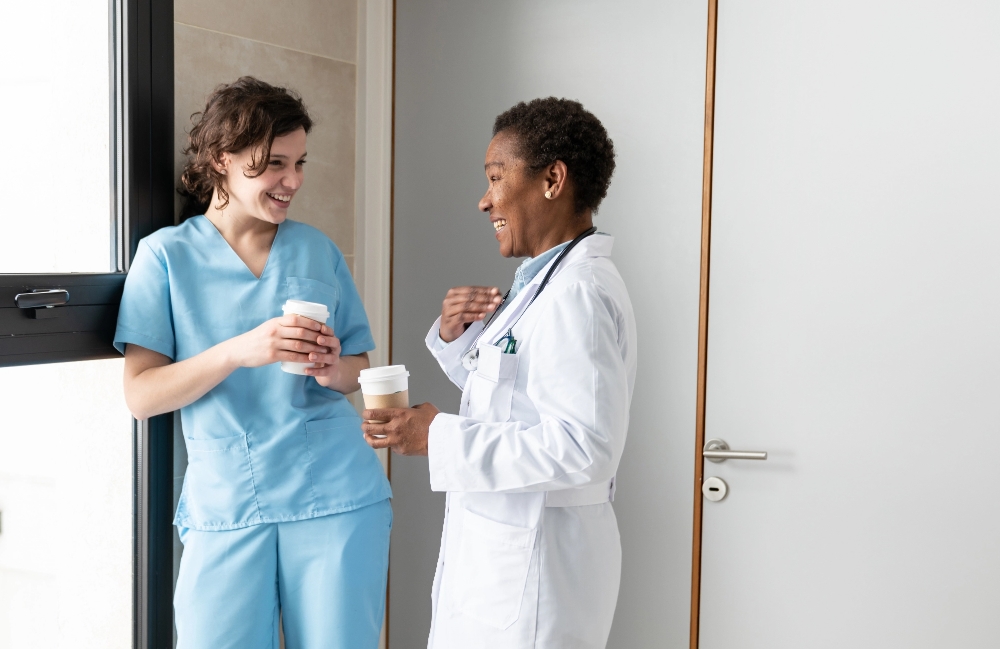 Two nurses smiling as they hold coffee cups