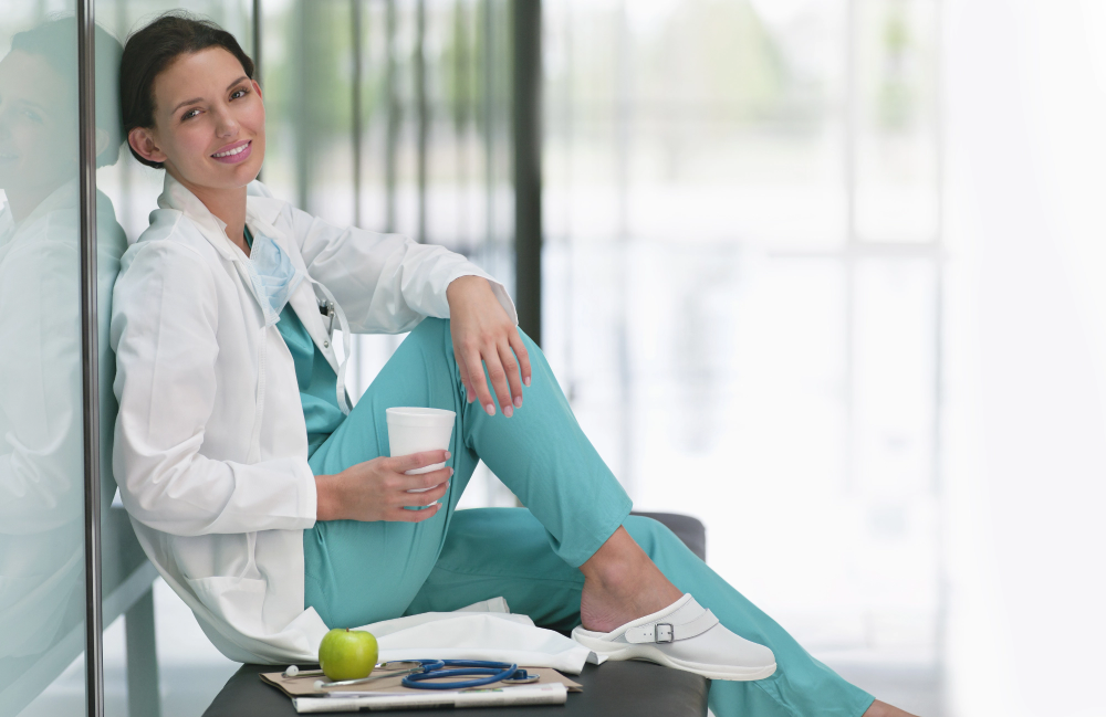 Nurse relaxing against a wall with a cup of water in her right hand