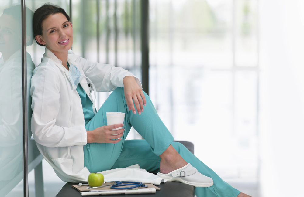 Nurse leaning against a wall with a cup of water in her right hand