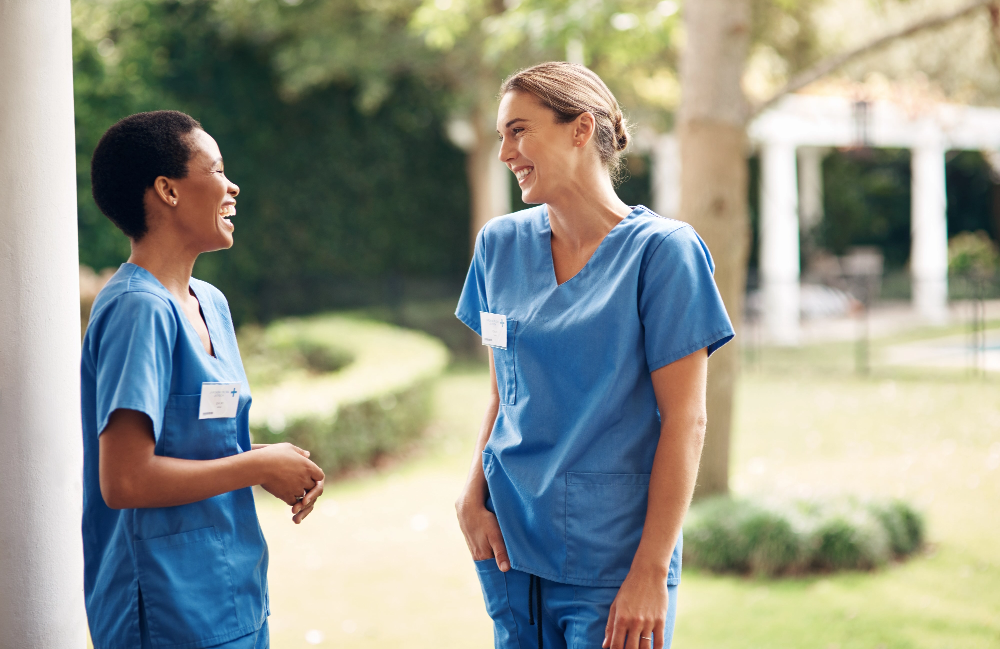 Two nurses smiling and having a conversation outdoors