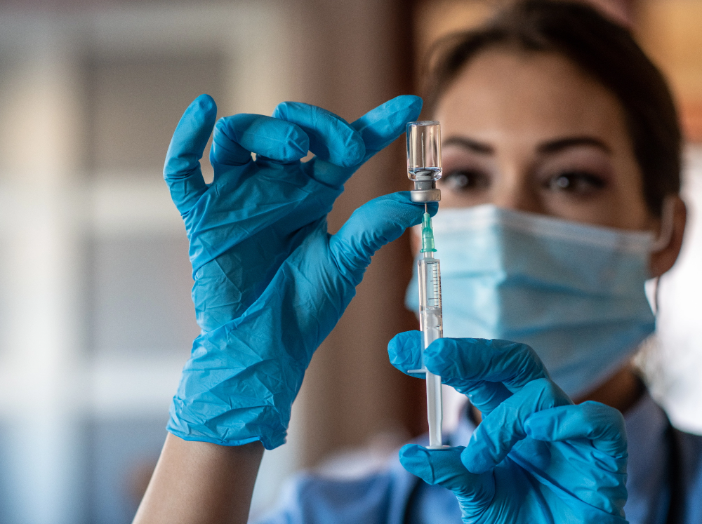 Woman wearing gloves inserting needle into vaccine vial