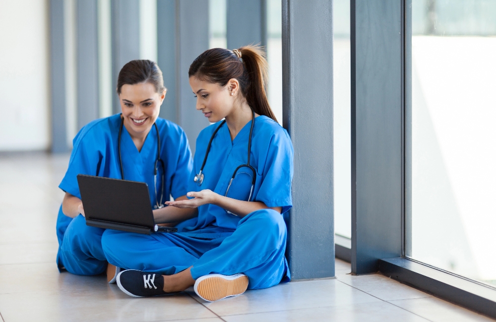 Two nurses seated on the floor with a laptop