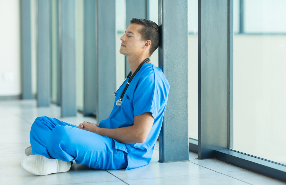 Nurse in blue leaning against a wall with his eyes closed