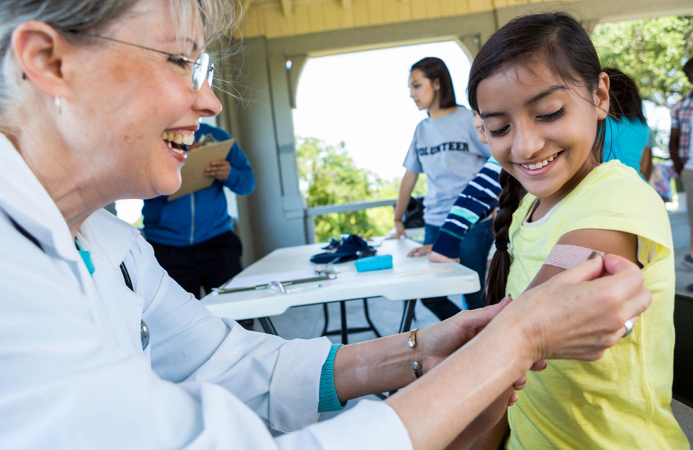 Smiling nurse placing a bandage on a girl's left arm outdoors