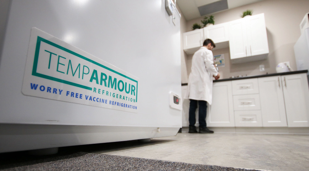 Man in a white lab coat working near a TempArmour vaccine refrigerator