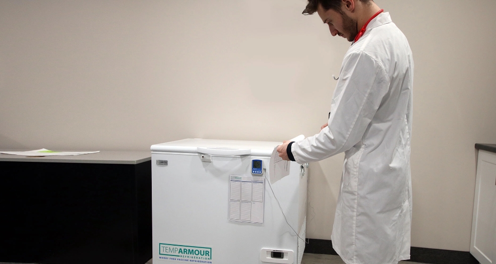 Man checking a data sheet while standing near a vaccine refrigerator