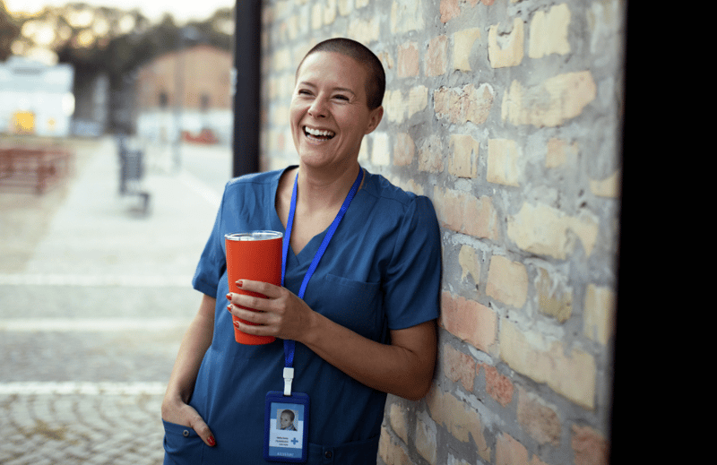 Smiling nurse leaning against a brick wall with a red cooler in her left hand